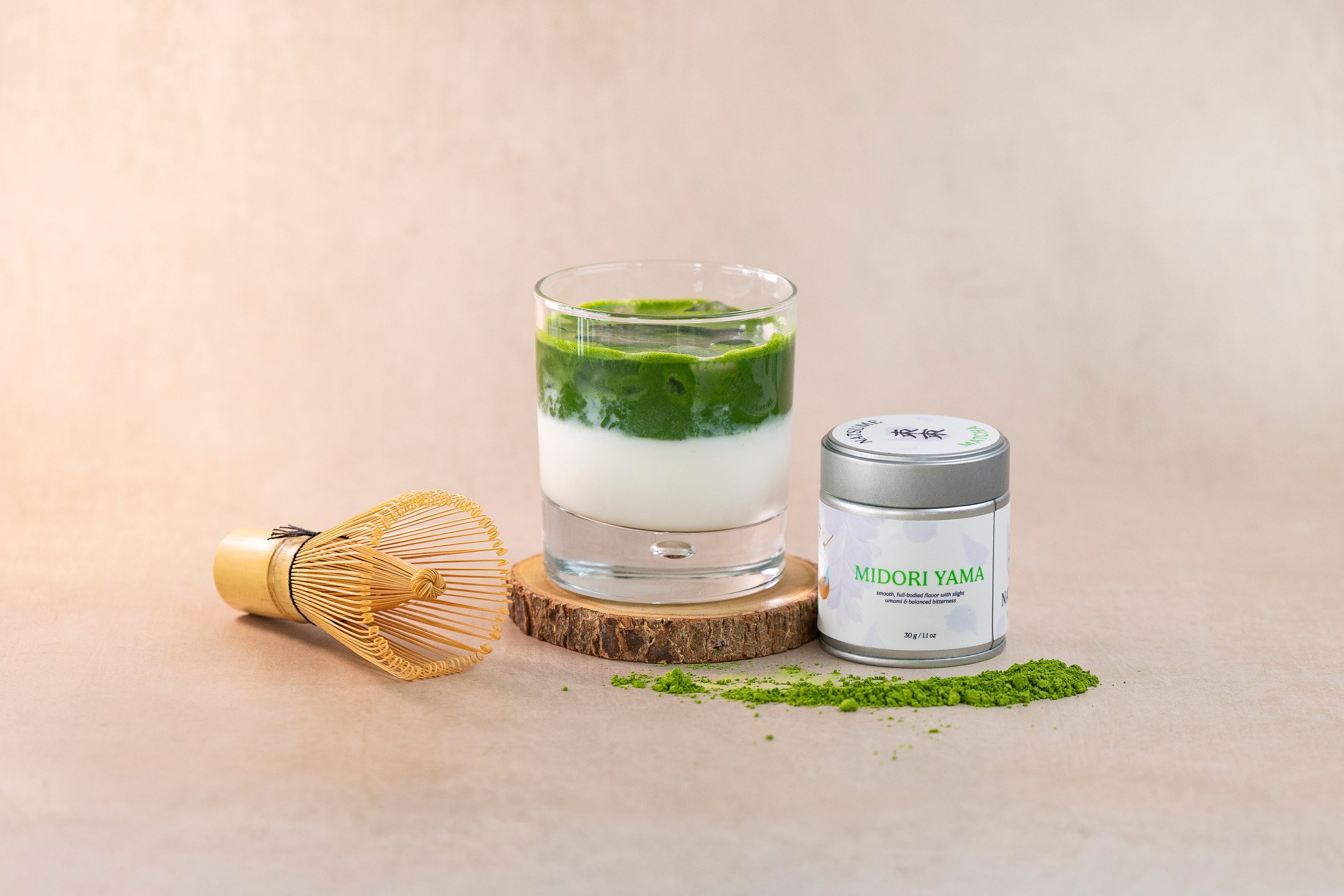 Matcha green tea with a glass, whisk, and container on a beige background
