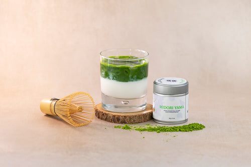 Matcha green tea with a glass, whisk, and container on a beige background