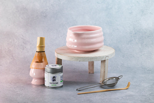 Matcha Tea-making set with a pink ceramic bowl, bottle, canister, and tools on a gray background