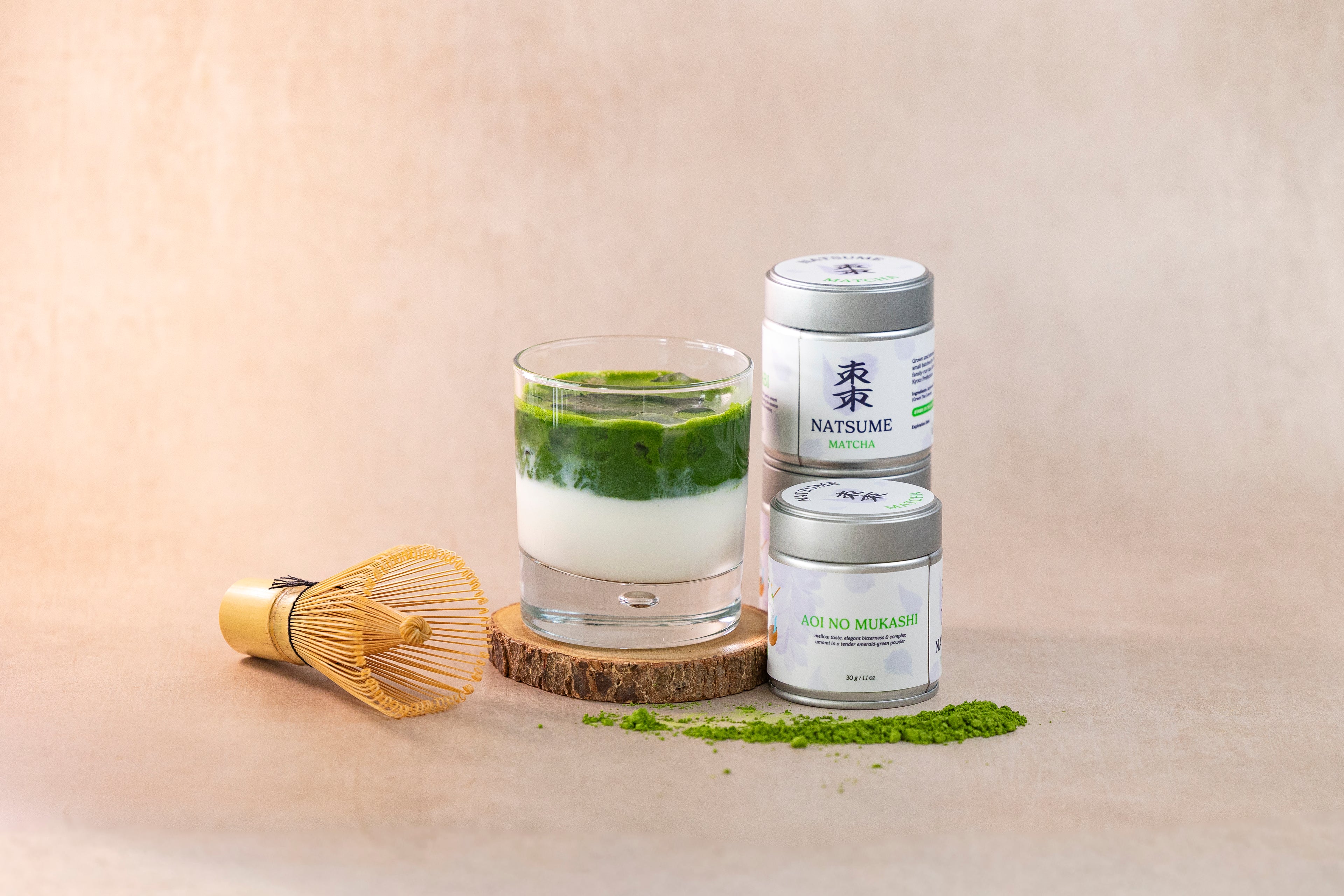 Matcha green tea latte with matcha powder canisters on a beige background with whisk