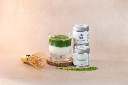 Matcha green tea latte with matcha powder canisters on a beige background with whisk