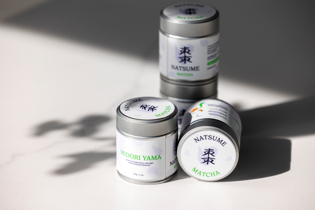 Four containers of Natsume matcha on a light surface with soft shadows.